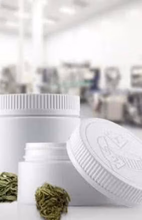 White ribbed plastic jars with lids and cannabis buds displayed in a manufacturing facility.