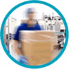 Circular icon showing a blurred healthcare worker in scrubs carrying a cardboard box in a clinical setting.