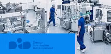 Workers in blue scrubs walk through a pharmaceutical production facility with automated packaging machinery.