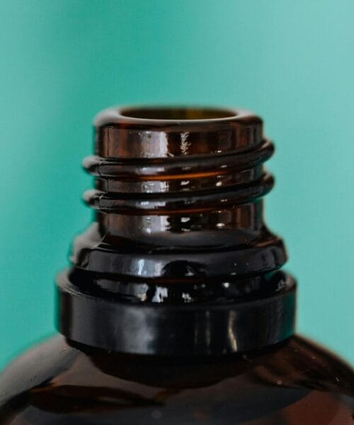 Close-up of an amber glass bottle's threaded neck against a teal background.